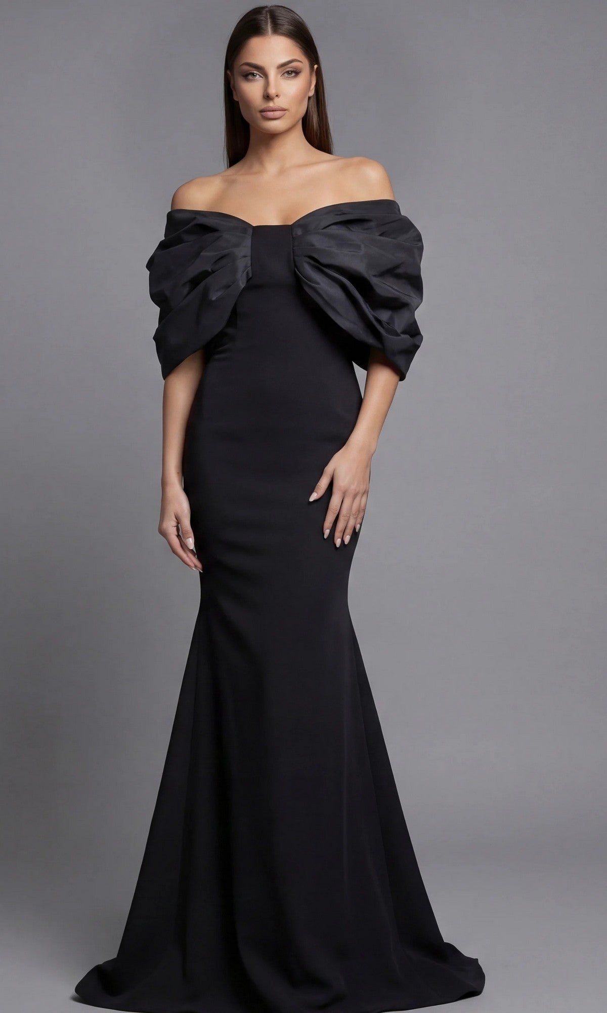 A woman stands against a gray background wearing the black Jovani 47657 long formal dress, featuring an off-the-shoulder neckline and dramatic ruffled sleeves.